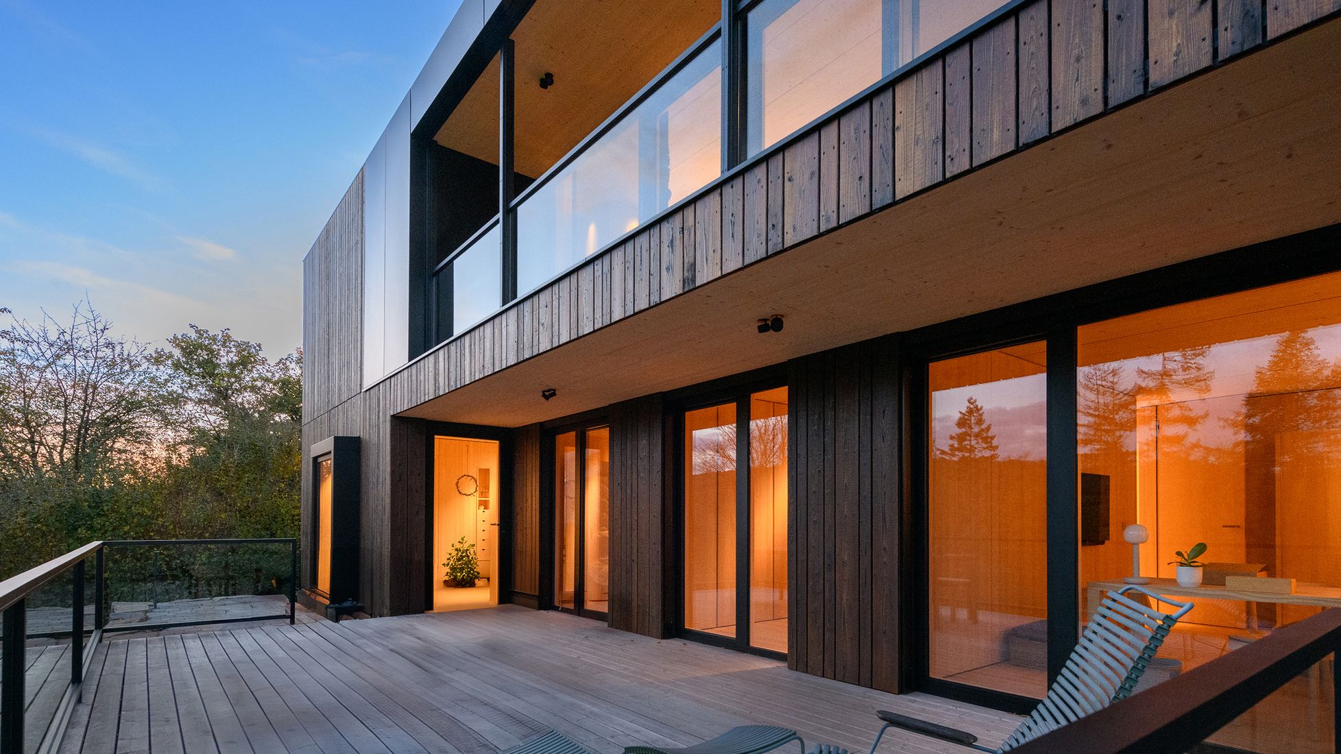 Modernes Wohngebäude mit großflächigen Glasfenstern und beleuchteter Terrasse bei Dämmerung